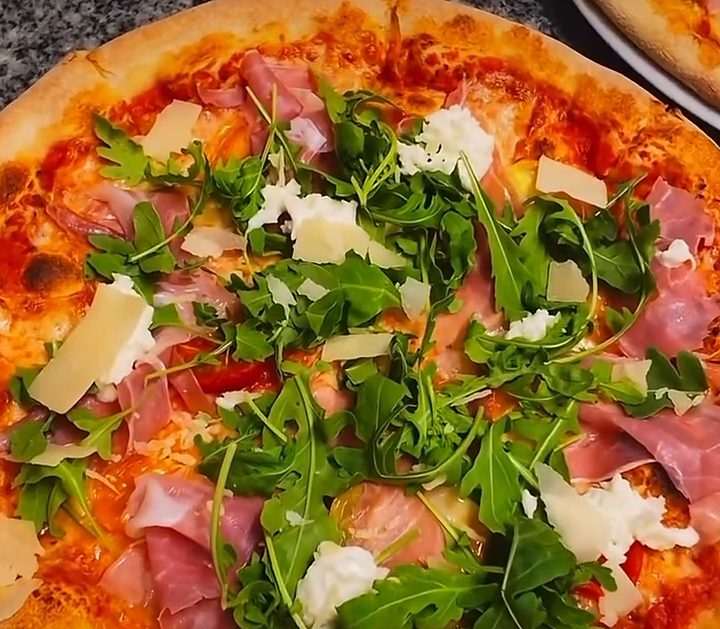 Pizza prosciutto di Parma met rucola en grana padano, net uit de oven